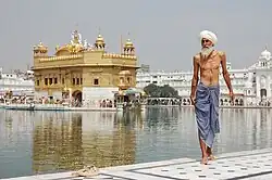 A Sikh pilgrim stands in the foreground, while in the background the Golden Temple (Harmandir Sahib) is plainly visible.